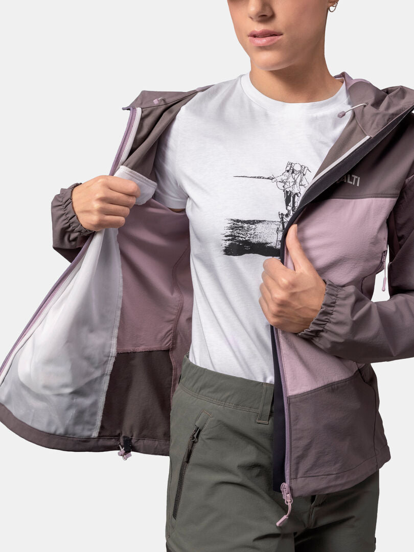 Person, die ein weißes bedrucktes T-Shirt und eine grüne Hose trägt und eine Halti Pallas Evo X-stretch-Jacke Damen auszieht.