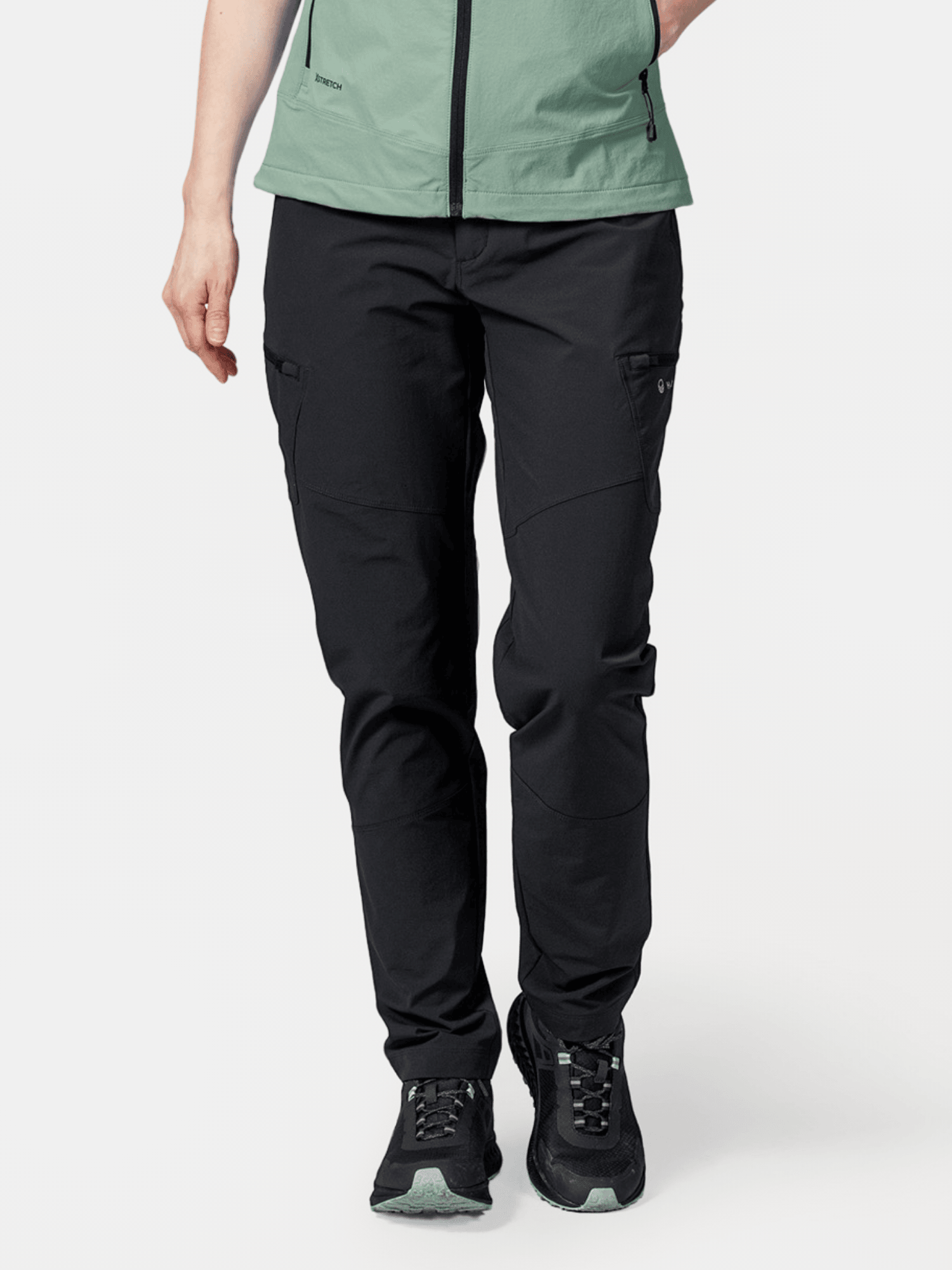 Eine Person trägt Halti Pallas Evo X-Stretch-Hosen Damen in Schwarz, mit einer hellgrünen Jacke und schwarzen Sneakers.