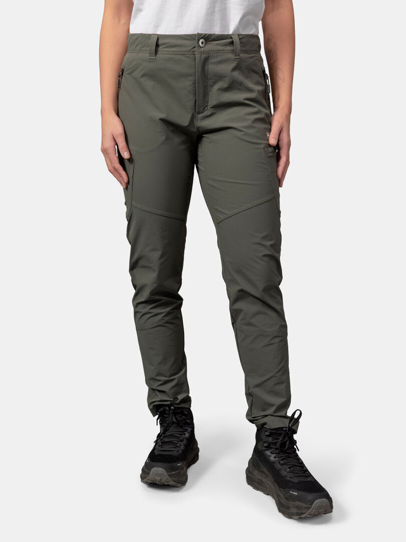 Person trägt Halti Pallas Evo X-Stretch-Hosen Damen, schwarze Wanderschuhe und ein weißes Hemd vor einem einfarbigen Hintergrund.