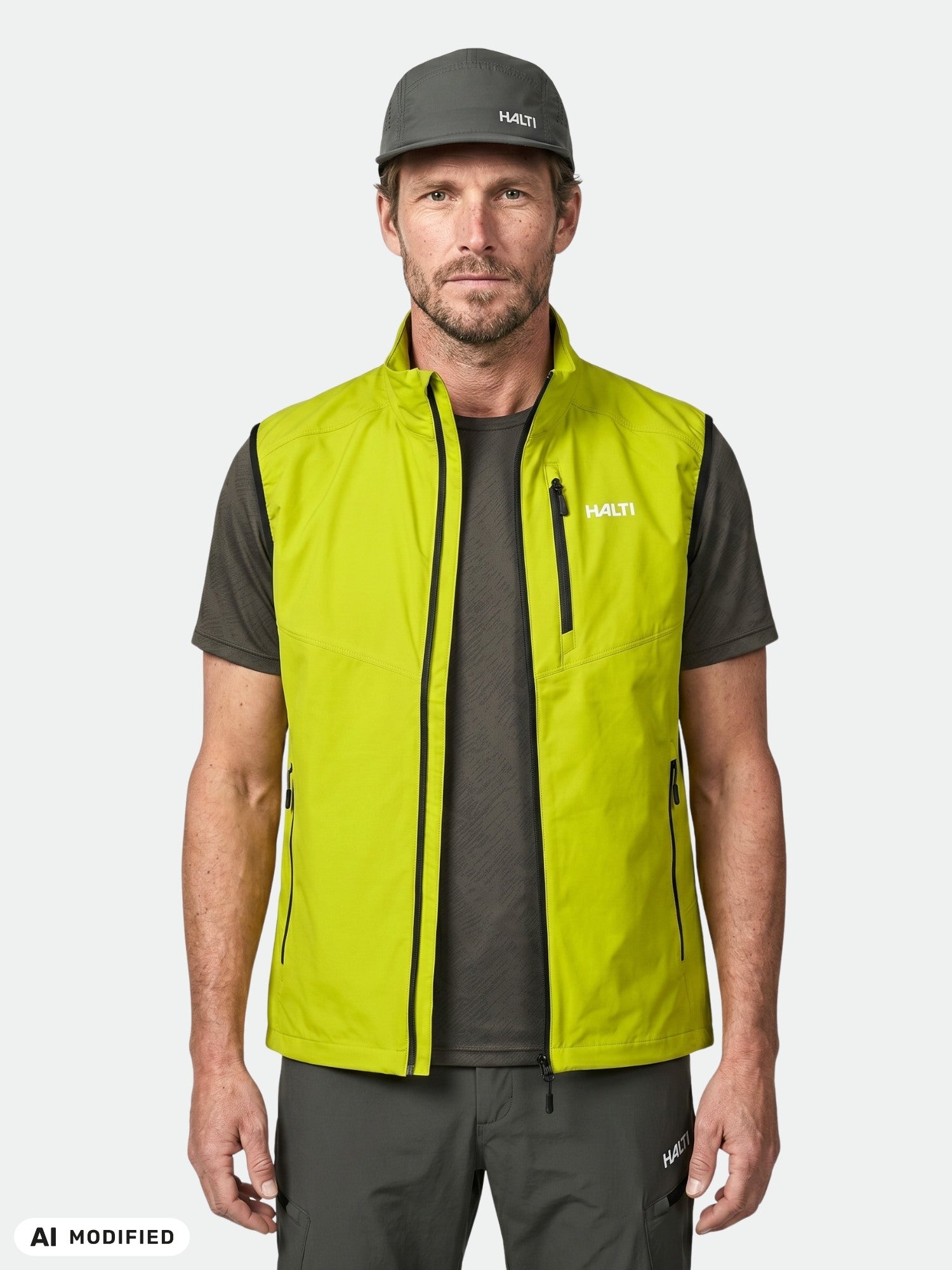 Ein Mann in einer „Halti Pallas Evo X-Stretch“-Weste für Herren, einem dunklen Hemd und einer Mütze steht mit dem Blick nach vorne vor einem weißen Hintergrund.