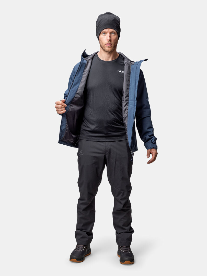 Ein Mann in Outdoor-Kleidung schaut nach vorne und trägt eine Halti Forter DX Warm Regenjacke Herren, Mütze, T-Shirt, Hose und Wanderschuhe.