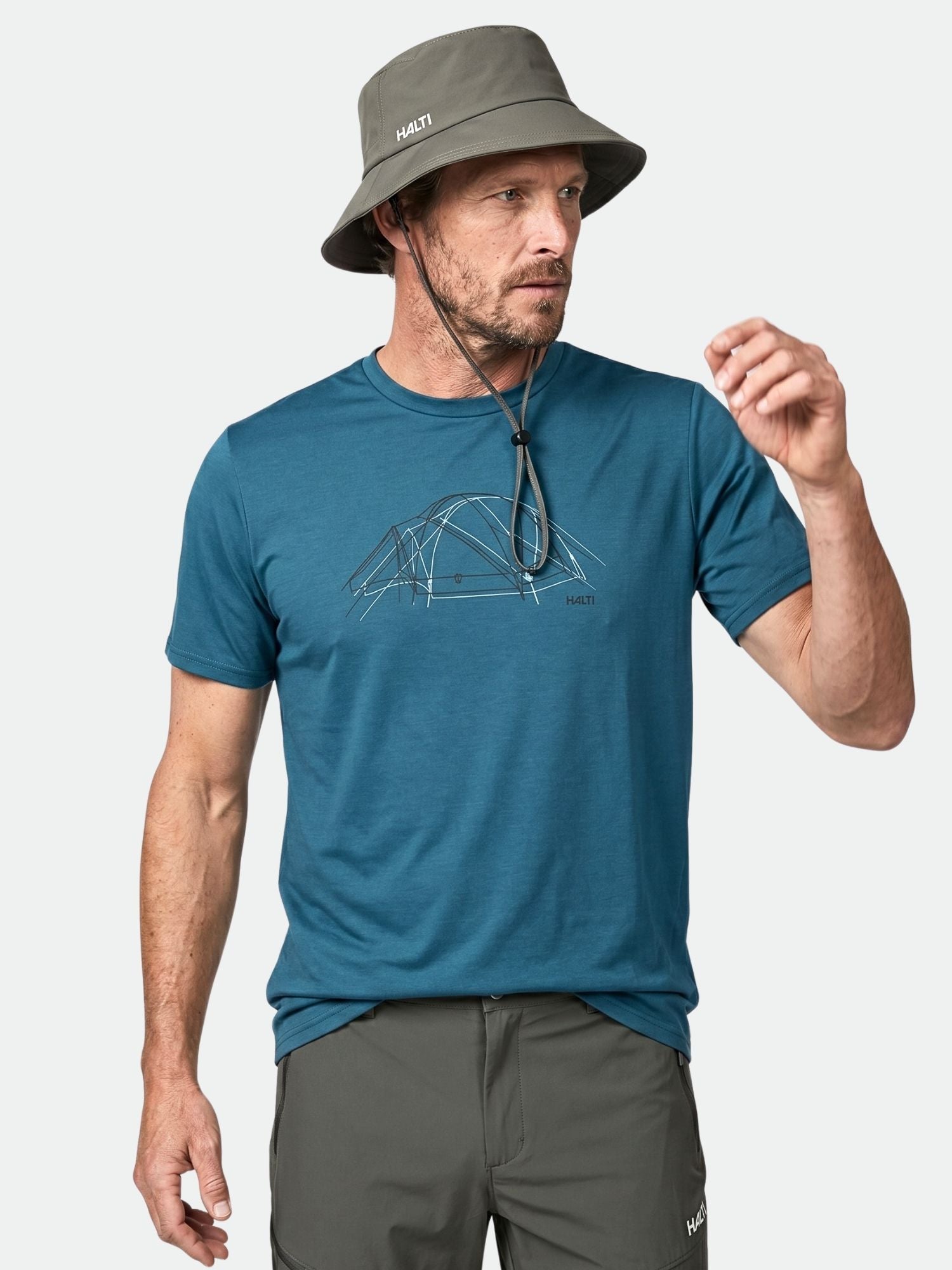 Mann in Halti Kalteva T-Shirt Herren mit Zeltgrafik, grauem Eimerhut und Hose, bereit für Outdoor-Aktivitäten.