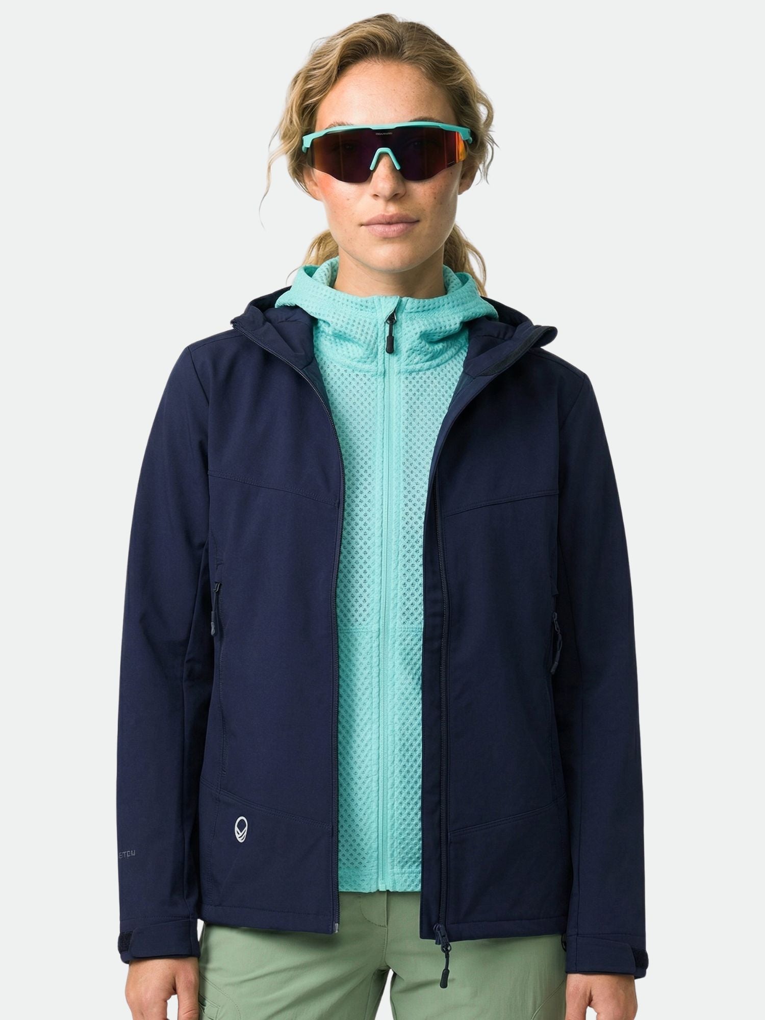 Eine Person mit Sonnenbrille und einer Halti Pallas Evo Brushed X-stretch Jacke Damen steht vor einem schlichten Hintergrund.