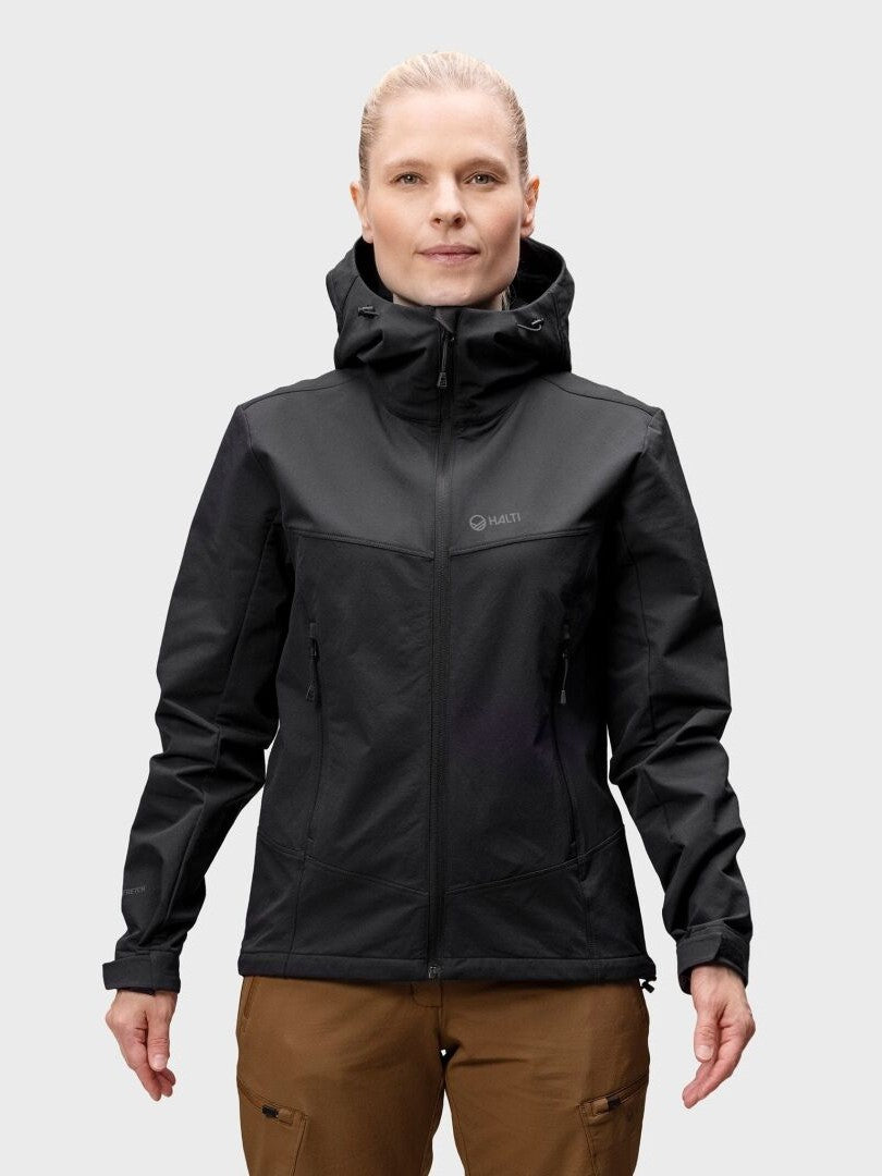 Person, die eine Halti Pallas Evo Brushed X-stretch Jacke Damen und eine braune Hose trägt, stehend vor einem hellgrauen Hintergrund.