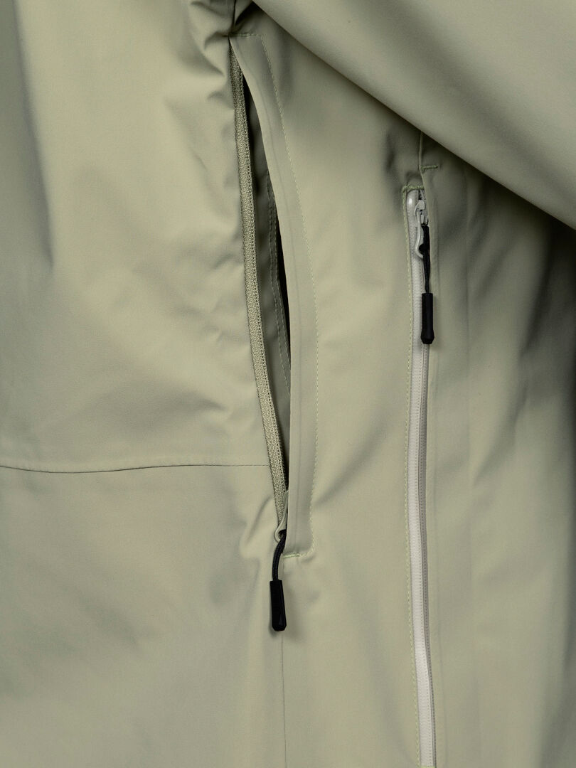 Nahaufnahme der Halti Staala DX Regenjacke für Damen mit einer teilweise geöffneten Reißverschlusstasche und glattem, wasserabweisendem Material.