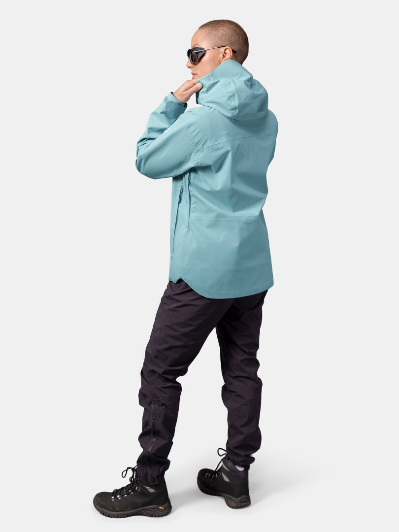 Eine Person mit Sonnenbrille trägt eine hellblaue Halti Staala DX Regenjacke Damen und eine schwarze Hose und schaut von der Kamera weg.
