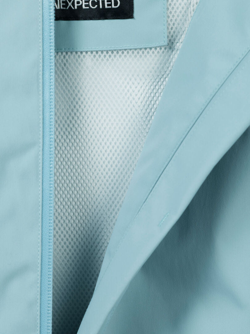 Nahaufnahme der Halti Staala DX Regenjacke Damen Plus, einer hellblauen, wasserabweisenden Jacke mit Mesh-Futter und Label-Detail.