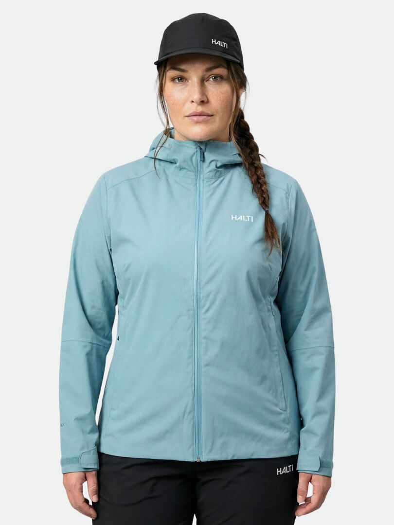 Eine Person mit einem Zopf trägt die hellblaue Halti Staala DX Regenjacke Damen Plus und eine schwarze Hose, bereit zum Trekking.