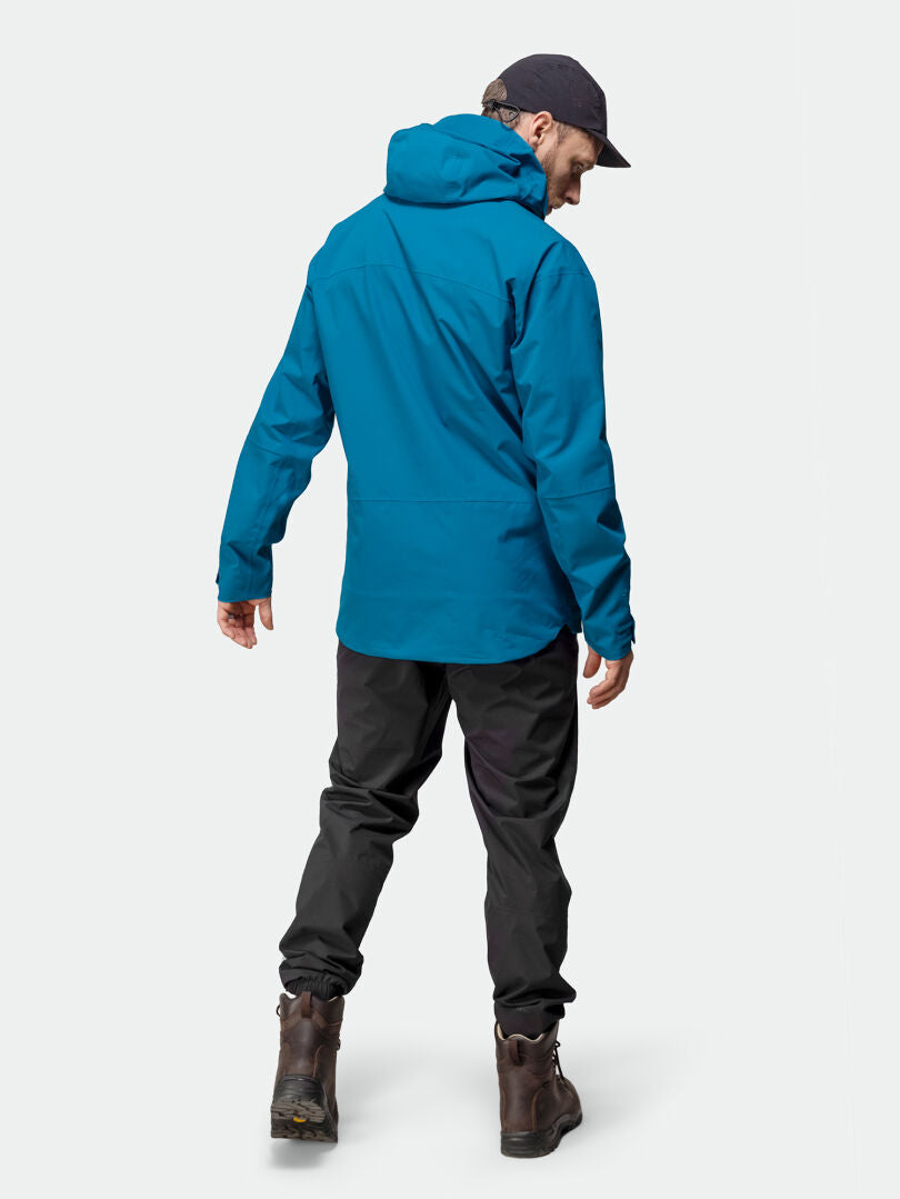Ein Mann in einer blauen Halti Staala DX Regenjacke Herren und einer schwarzen Hose, bereit für ein Outdoor-Abenteuer, von hinten gesehen.