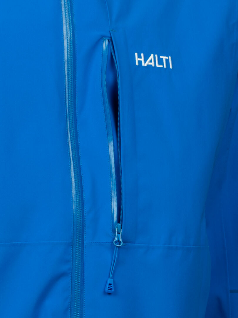 Nahaufnahme der Halti Staala DX Regenjacke Herren, einer blauen wasserdichten Jacke mit Brusttasche mit Reißverschluss und weißem Logo.