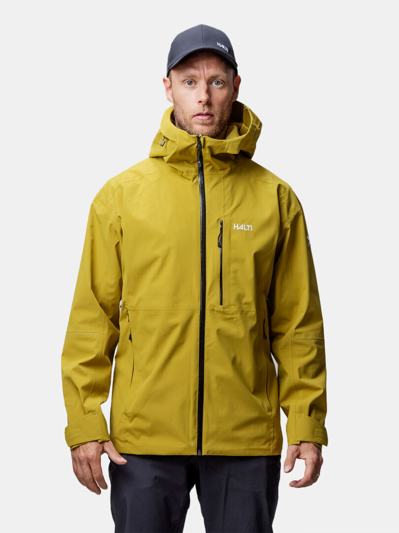 Ein Mann in einer gelben Halti Staala DX Regenjacke Herren und dunkler Mütze steht mit dem Gesicht nach vorne vor einem weißen Hintergrund.