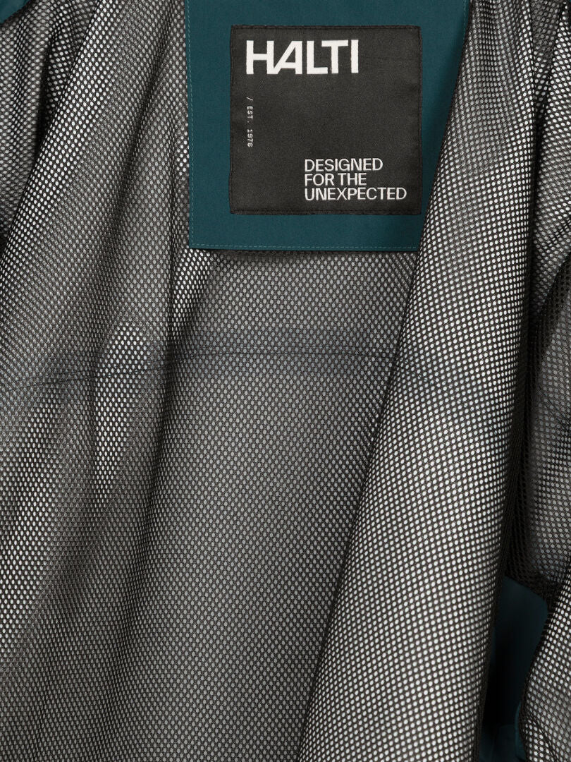 Nahaufnahme des Innenfutters der Staala DX Regenjacke für Herren mit einem Halti-Etikett, auf dem in weißer Schrift „DESIGNED FOR THE UNEXPECTED“ steht.
