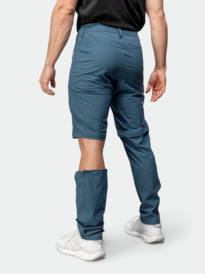 Eine Person, die Halti Pallas Cool Stretch Zip-off Hosen Herren mit einem abgenommenen Bein und weiße Turnschuhe trägt, von hinten gesehen.