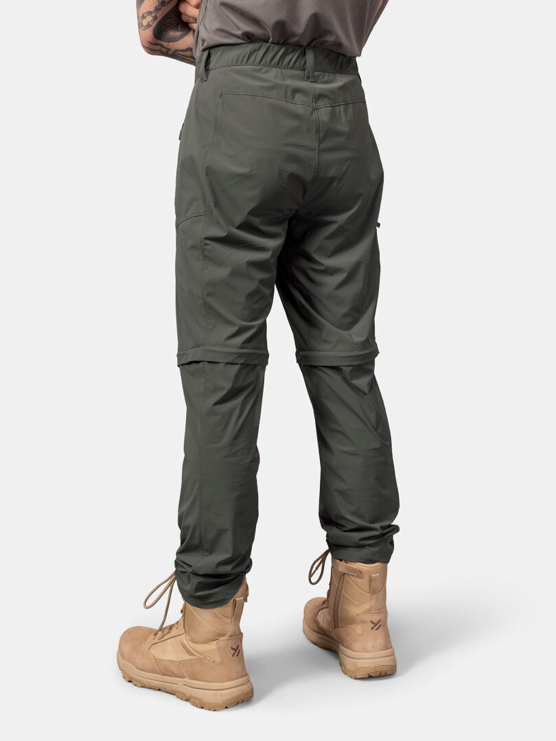 Eine Person trägt Halti Pallas Cool Stretch Zip-off Hosen Herren und hellbraune Stiefel, dargestellt von hinten auf einem schlichten hellen Hintergrund.