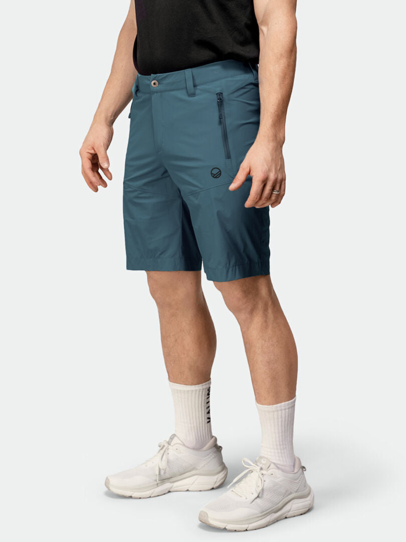 Eine Person trägt teal Halti Pallas Cool X-stretch Shorts Herren, ein schwarzes Hemd, weiße Socken und Turnschuhe.