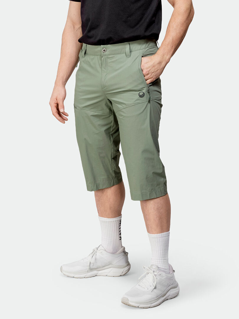 Eine Person in Halti Pallas Cool X-Stretch Caprihose Herren, schwarzem T-Shirt, weißen Socken und Turnschuhen.