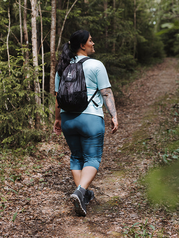 Eine Person mit Rucksack wandert im Wald und trägt die Halti Pallas Cool X-Stretch Caprihose Damen Plus mit UPF 90+.