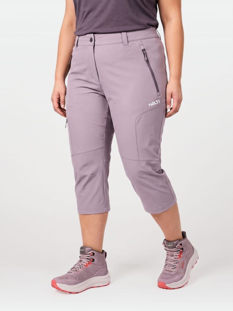 Eine Person in Halti Pallas Cool X-stretch Caprihose Damen Plus, dunklem Hemd und grauen Wanderschuhen mit rosa Akzenten.