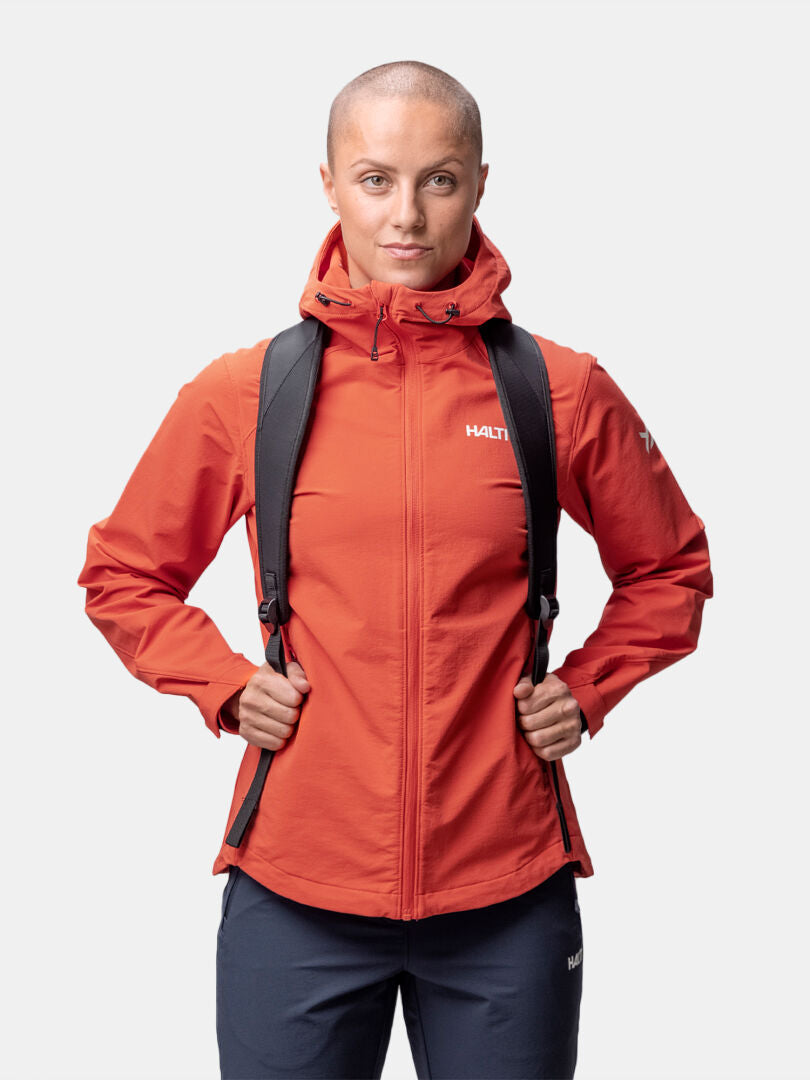 Eine Person in einer Halti Finholma X-stretch Jacke Damen und schwarzem Rucksack steht vor einem schlichten weißen Hintergrund.