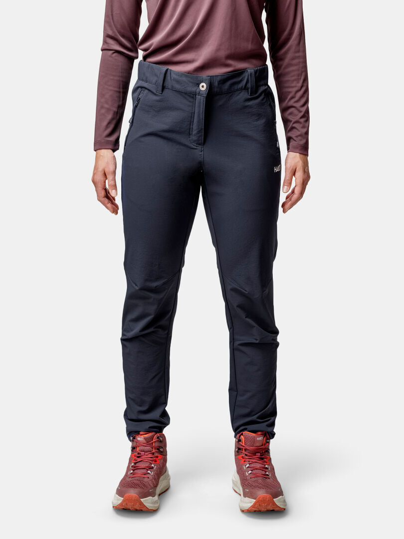 Person trägt die Halti Finholma X-stretch Hose Damen, langes Maroonshirt und rote Sneaker vor schlichtem Hintergrund.