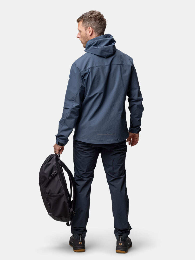 Ein Mann in einer blauen Halti Finholma X-Stretch Jacke Herren steht im Freien und trägt einen schwarzen Rucksack.