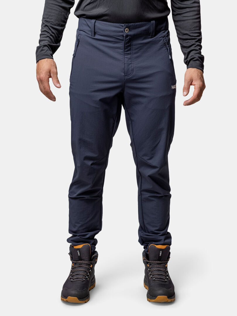 Ein Mann in marineblauer Halti Finholma X-Stretch-Hose, schwarzem Langarmshirt und Wanderschuhen steht mit dem Gesicht nach vorne.