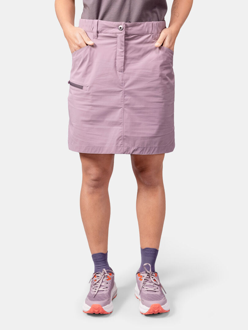 Person mit Halti Pallas Cool Rock Damen, lila Socken, Turnschuhen, Hände in den Taschen, vor einfarbigem Hintergrund.