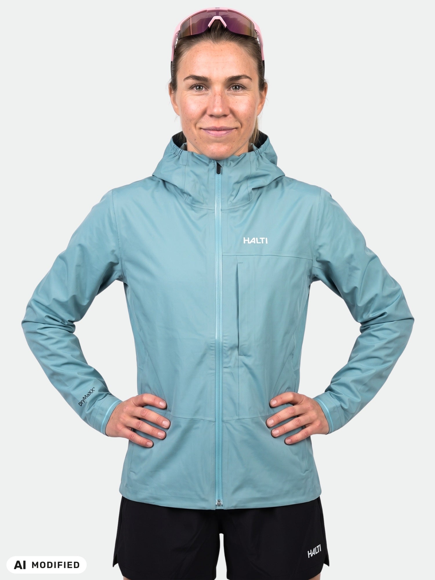 Eine Person in einer Halti Taival DX 3L Damenjacke (hellblau) und schwarzen Shorts steht mit den Händen in den Hüften und blickt nach vorne.