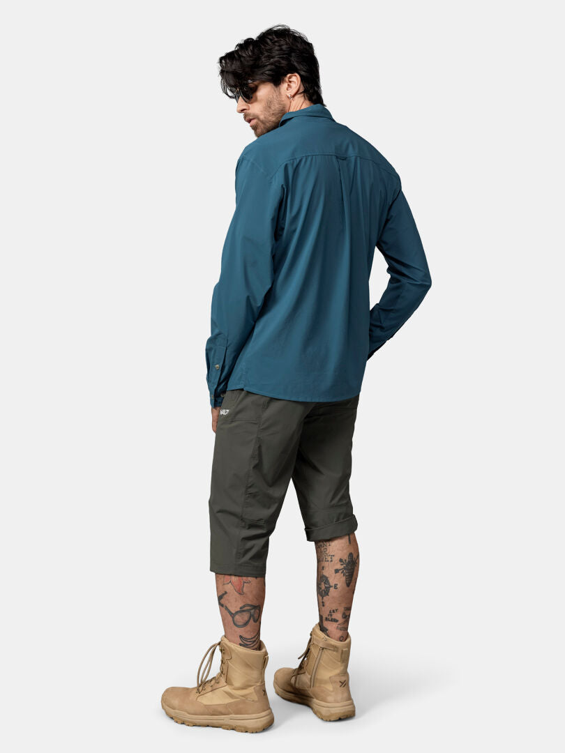Ein Mann in einem blauen Halti Samoy Langarm Funktionshemd (UPF 90+) und olivfarbenen Shorts ist bereit für Aktivitäten im Freien.