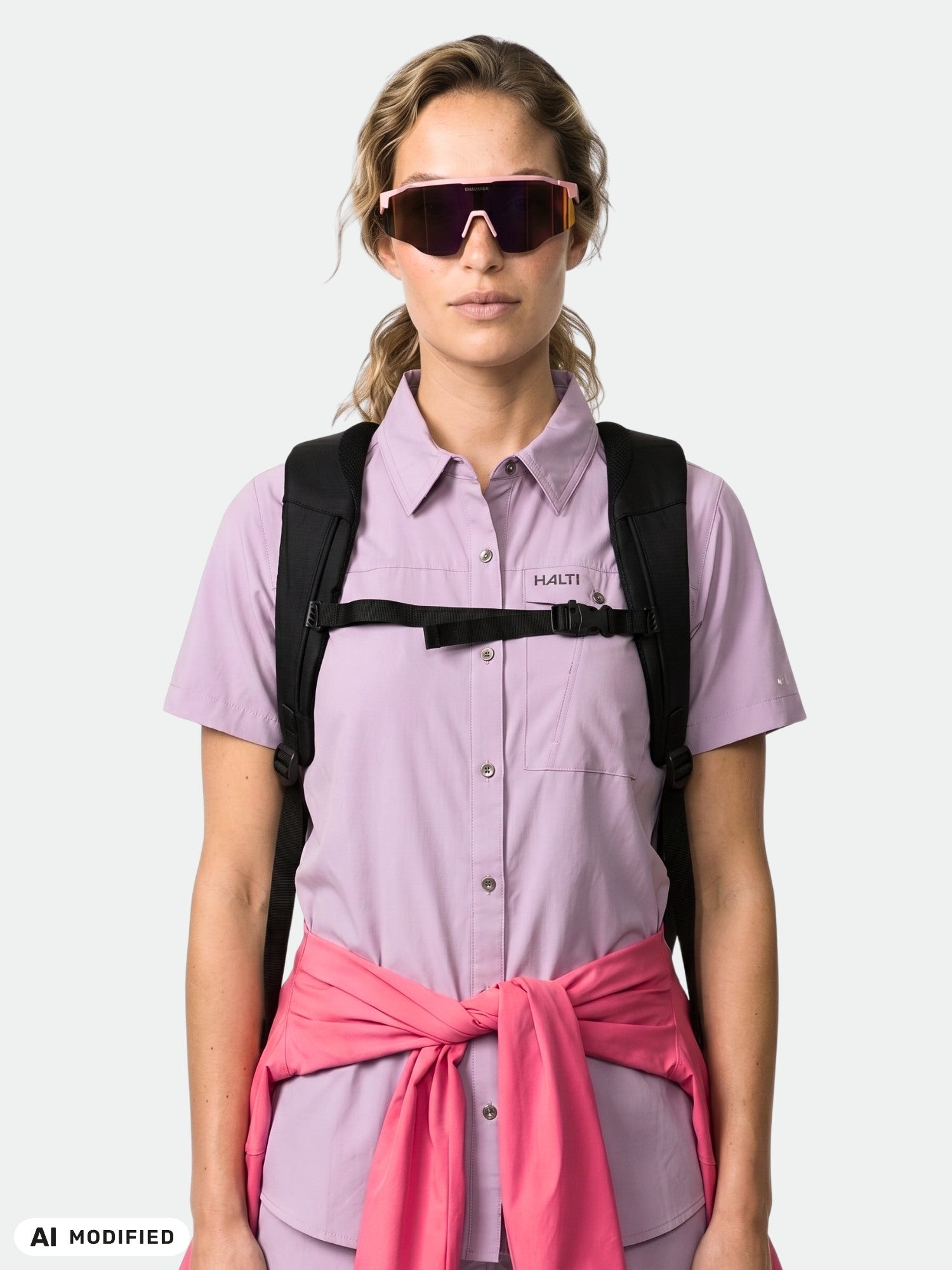 Jemand mit Sonnenbrille, dem lila „Halti Samoy Funktionshemd Damen“, Rucksackträgern und einem rosa Pullover.