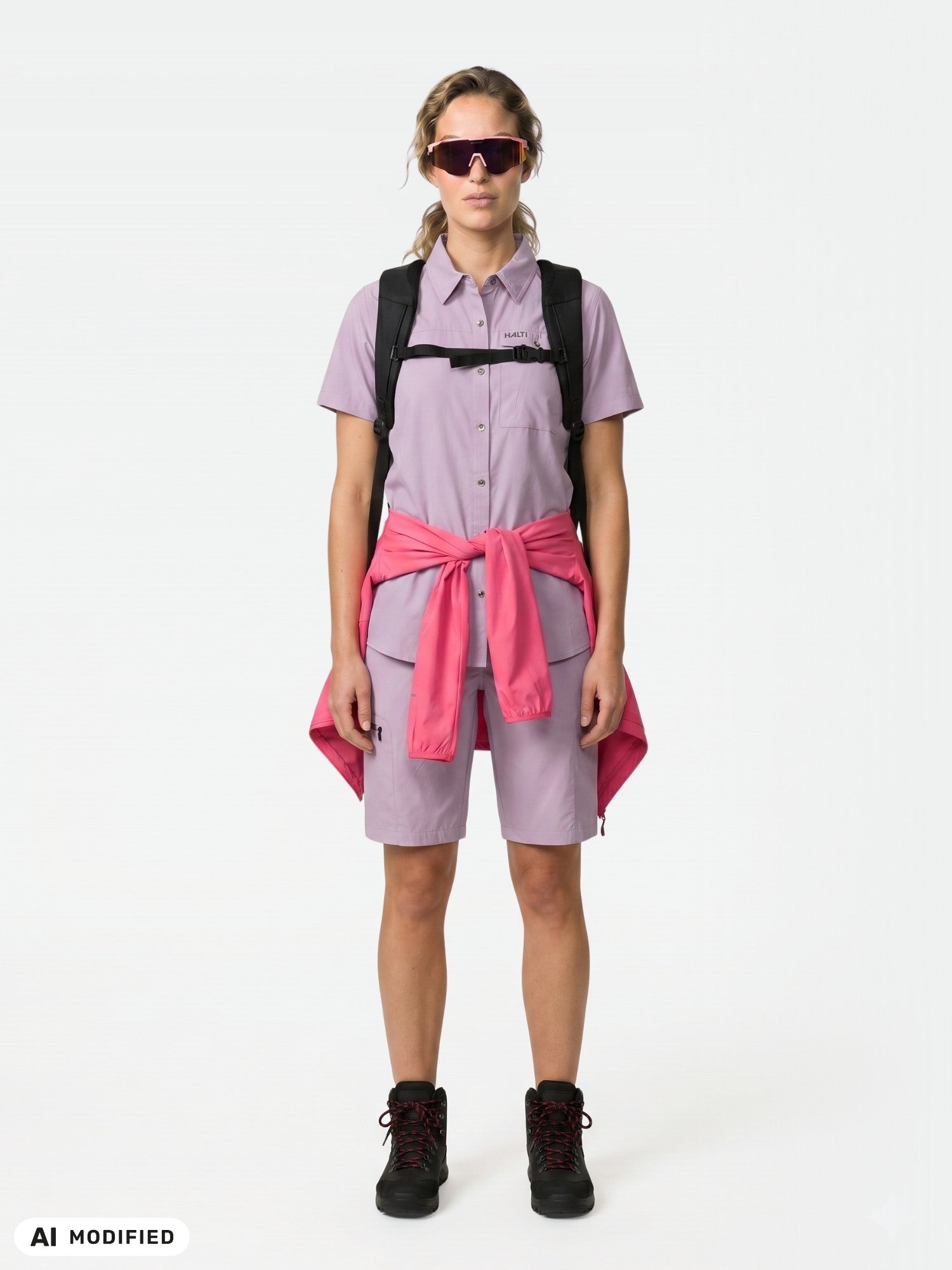 Person in einem violetten Halti Samoy Funktionshemd, schwarzen Stiefeln, Sonnenbrille und einer rosa Jacke, die bis zur Taille reicht; aus schnelltrocknendem Material.