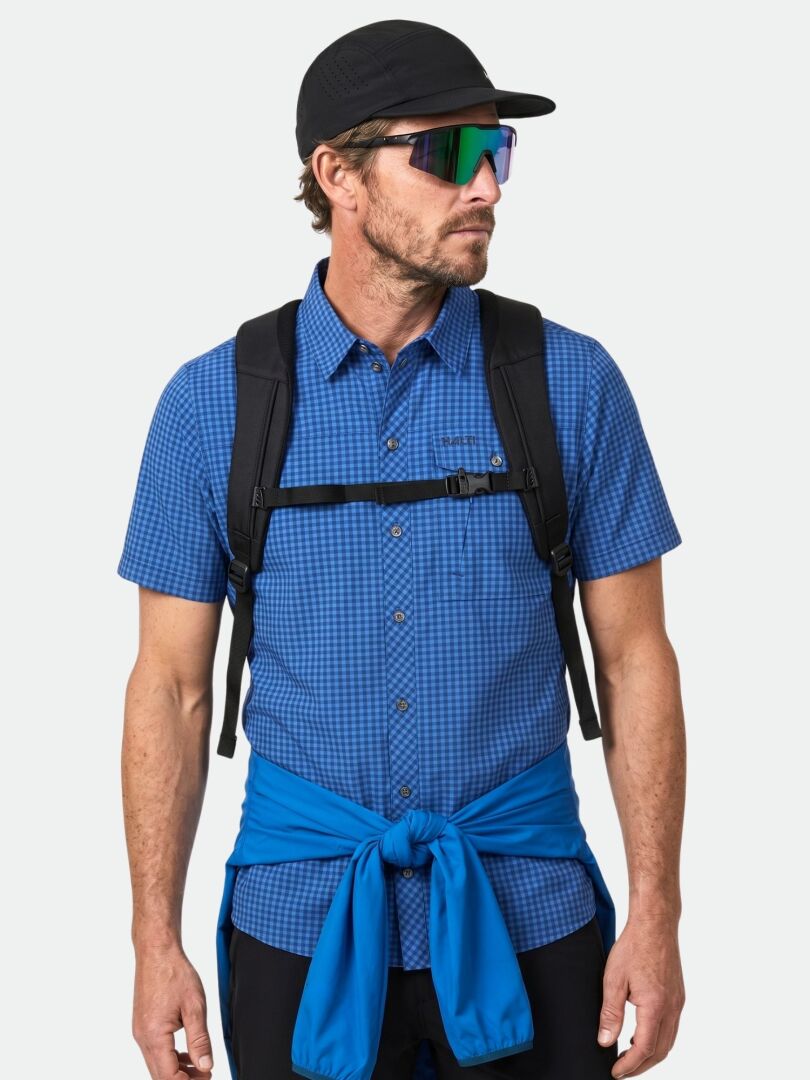 Mann mit Sonnenbrille, schwarzer Mütze, Rucksack und Halti Samoy Funktionshemd Herren mit blauer Jacke, die in der Taille gebunden ist.