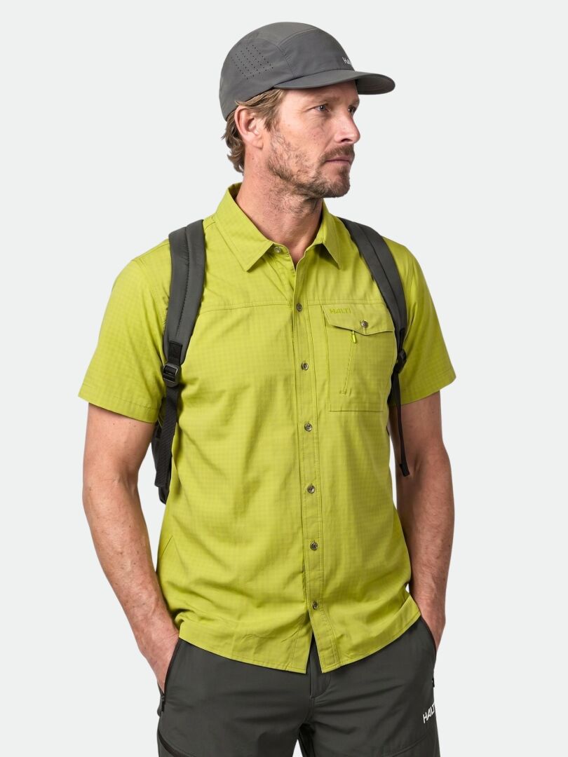 Mann in Halti Samoy Funktionshemd Herren, graue Hose, graue Mütze, und schwarzer Rucksack steht Hände in Taschen.
