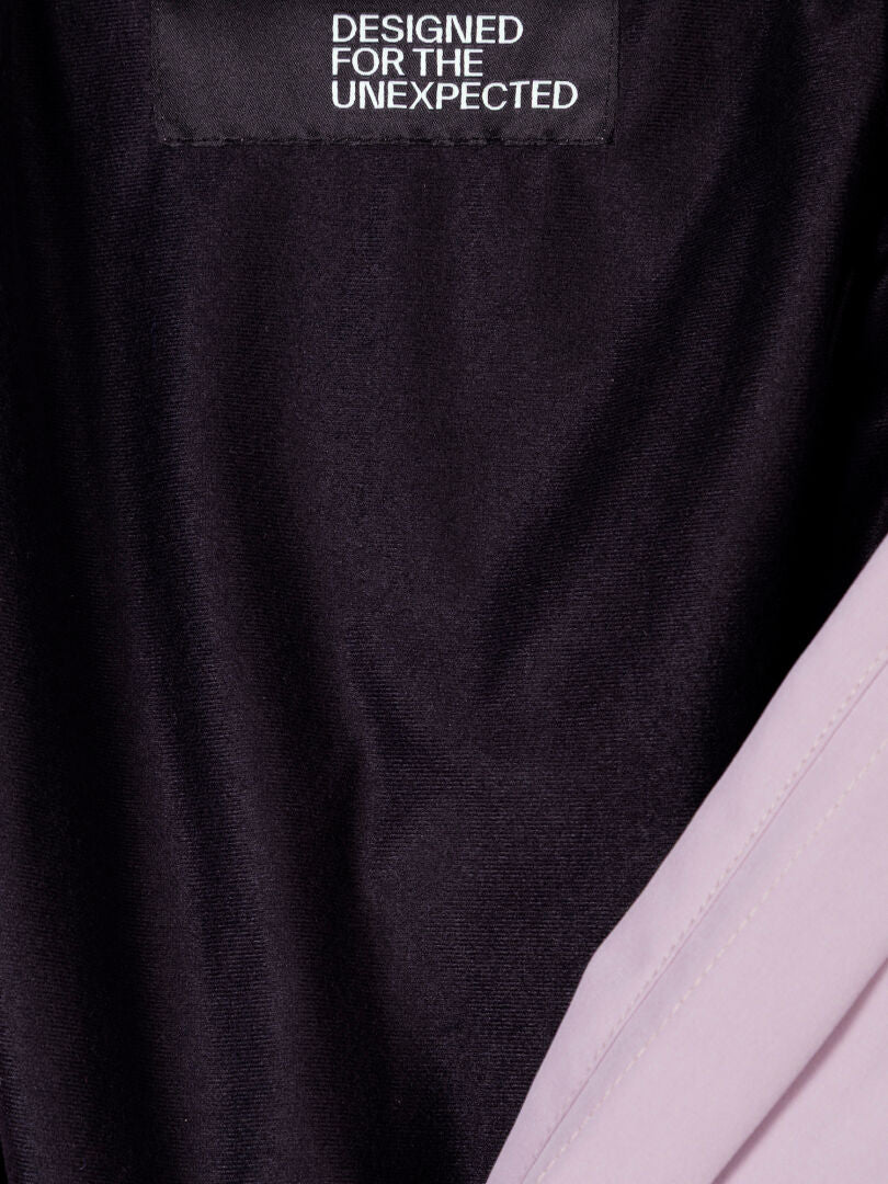 Nahaufnahme des schwarzen Halti-Etiketts mit der Aufschrift DESIGNED FOR THE UNEXPECTED im Inneren einer Valaja DX Parkajacke Damen, hellviolettes Futter.