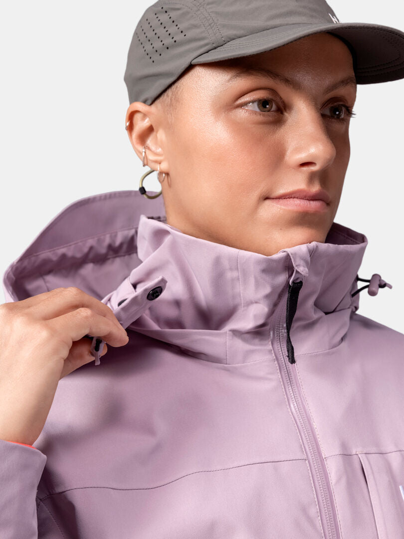 Person, die eine graue Mütze und eine hellviolette Halti Valaja DX Parkajacke Damen trägt und den Jackenkragen verstellt.