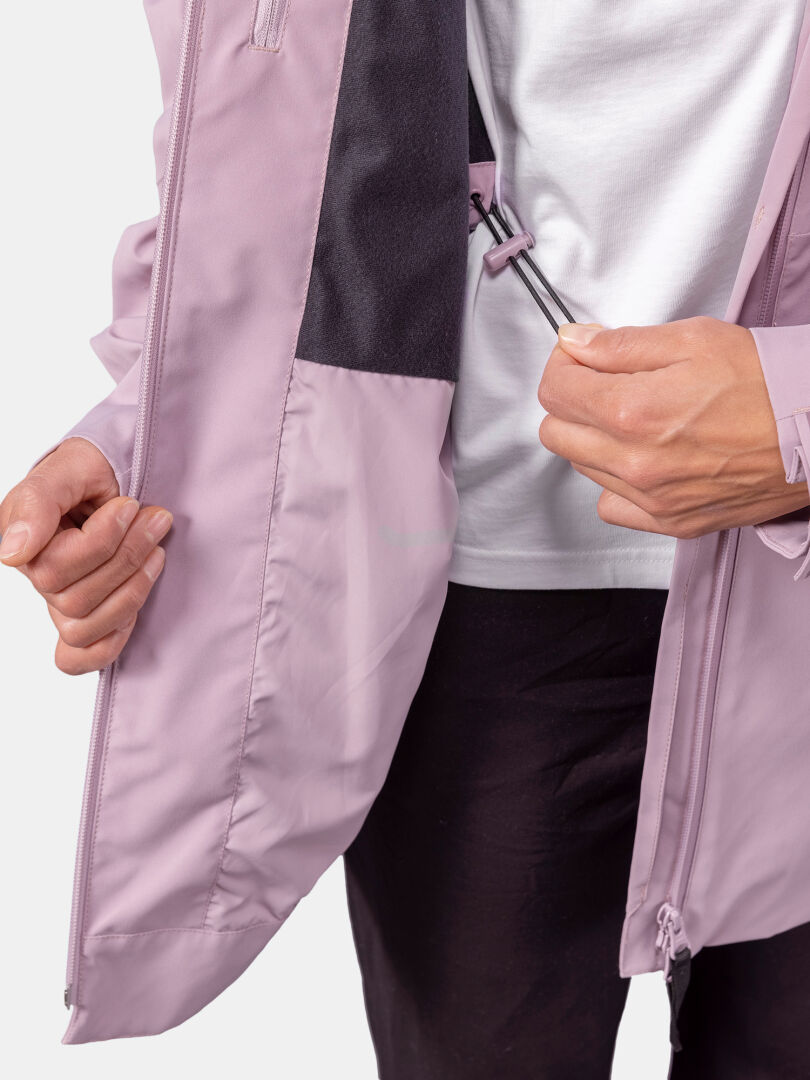 Jemand zieht den inneren Kordelzug einer hellvioletten Halti Valaja DX Parkajacke Damen über einem weißen Hemd und einer schwarzen Hose zurecht.