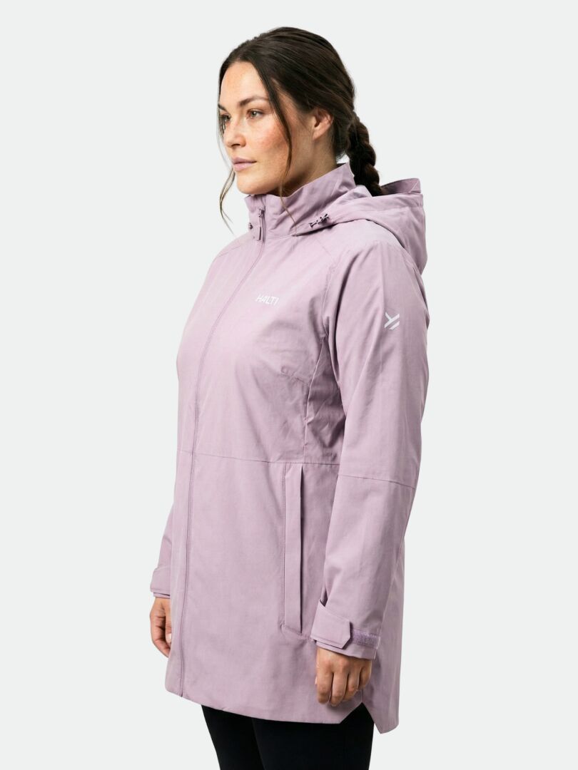 Frau in einer hellvioletten Halti Valaja DX Parka Jacke Damen Plus, seitlich stehend vor einem hellgrauen Hintergrund.
