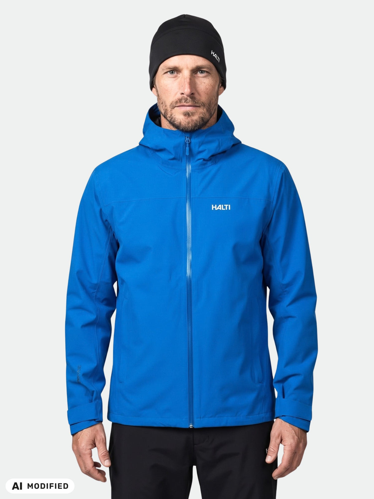 Ein Mann, der eine blaue Halti Kaltimo DX Regenjacke Herren mit Kapuze und eine schwarze Mütze trägt.