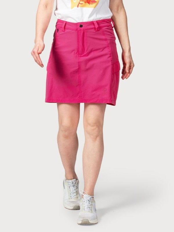 Person, die ein weißes T-Shirt, Halti Reissu Damen Stretch Rock in leuchtendem Pink und weiße Turnschuhe vor einem unifarbenen Hintergrund trägt.