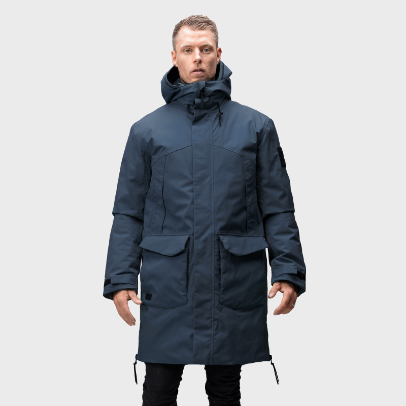 Eine Person in einem Halti Bergga DX Winter Parka Herren steht mit dem Gesicht nach vorne vor einem schlichten hellgrauen Hintergrund.