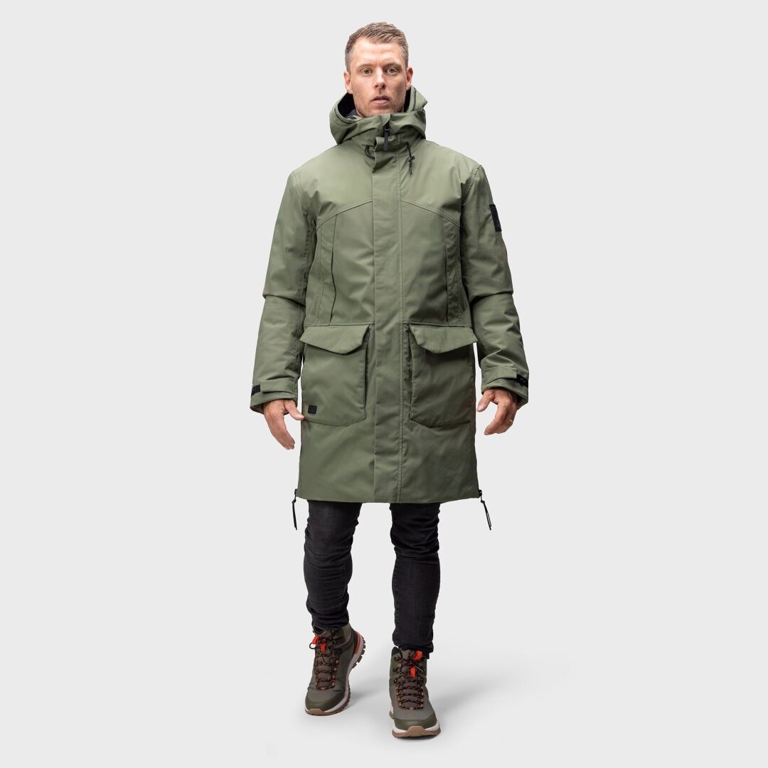 Ein Mann in einem Halti Bergga DX Winterparka, einer schwarzen Hose und Wanderschuhen steht mit dem Gesicht nach vorne vor einem schlichten Hintergrund.