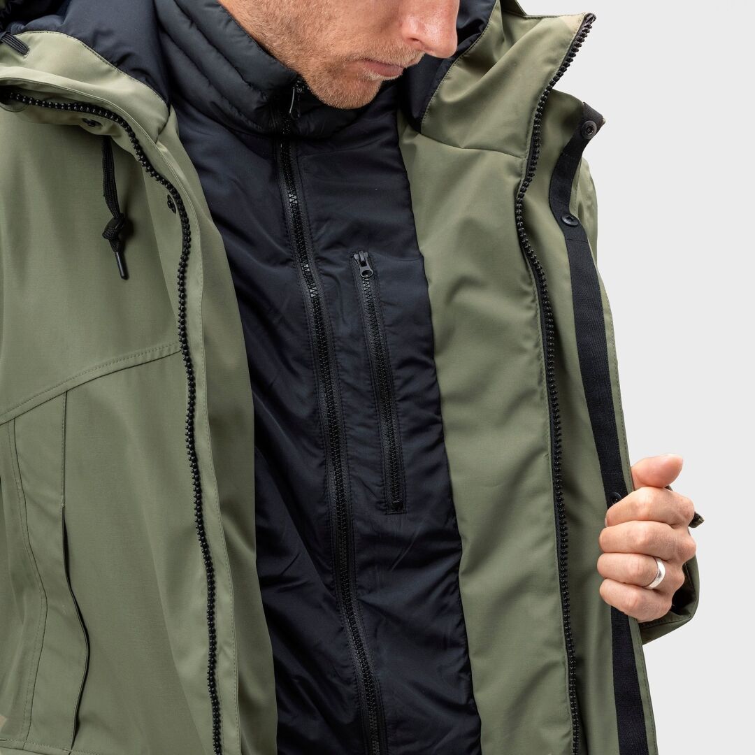 Eine Person in einem grünen Halti Bergga DX Winter Parka Herren über einem schwarzen Zip-up, die den Rand des Parkas offen hält.