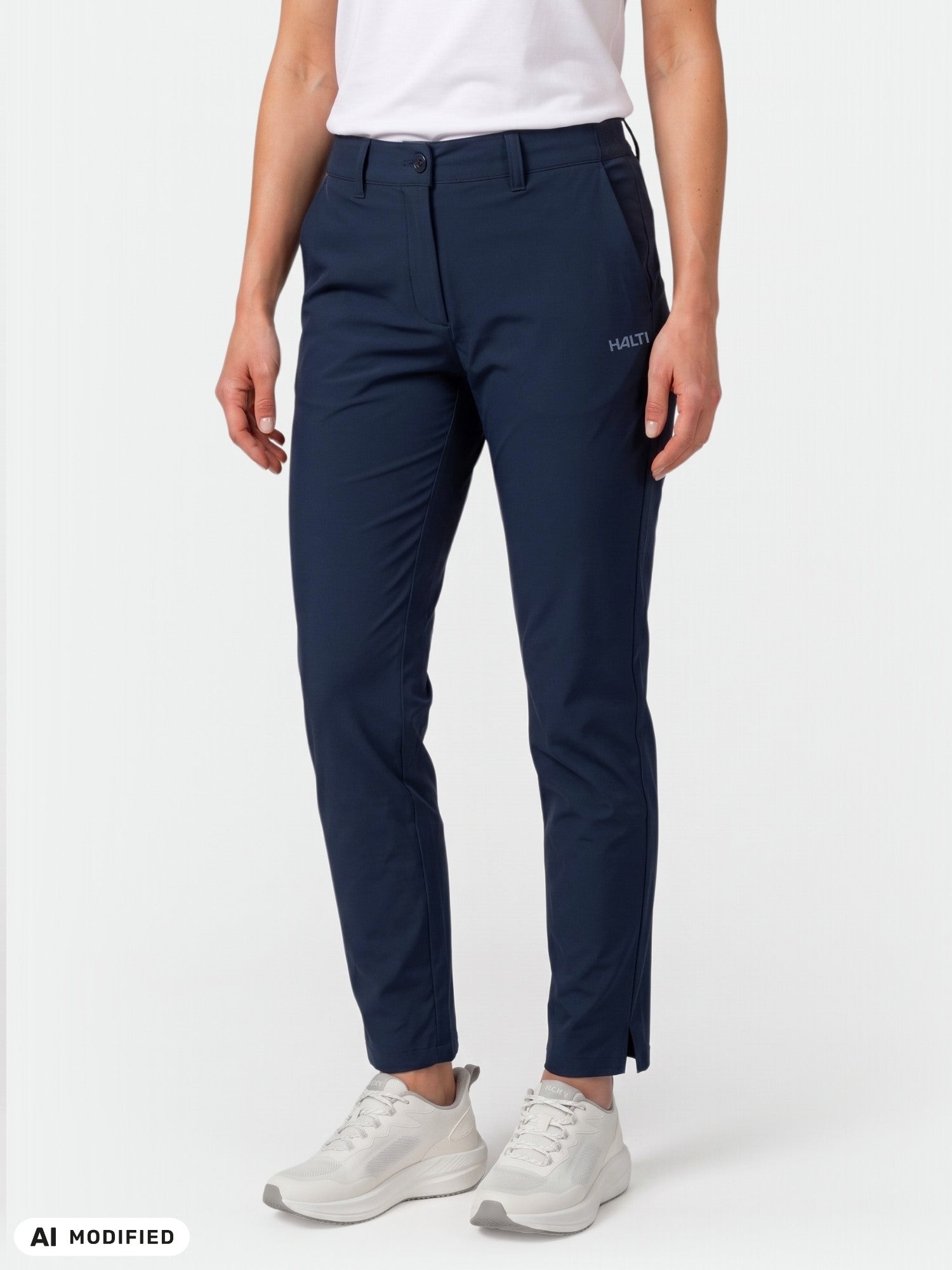 Das Model trägt eine „Halti Drive X-Stretch Chinos Damen“ in Marineblau, dazu ein weißes Hemd und Sneaker, vor einem hellen Hintergrund.