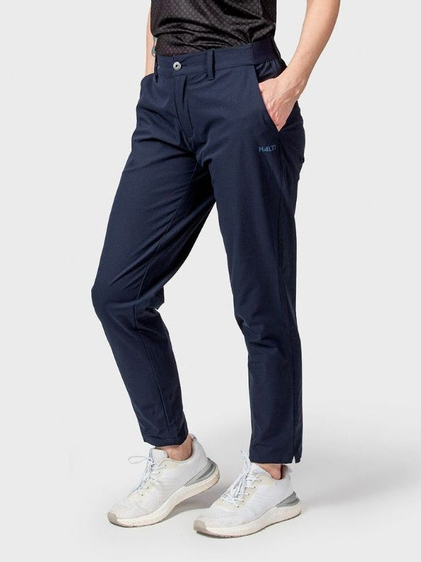 Person, die Halti Drive Damen X-stretch Chinos, ein schwarzes Hemd und weiße Turnschuhe vor einem einfarbigen Hintergrund trägt.
