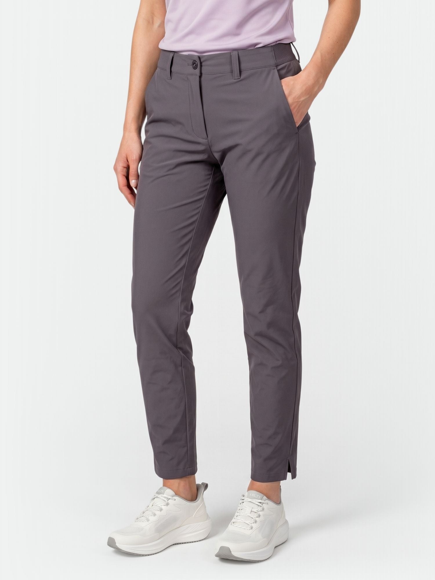 Sie trägt Halti Drive X-stretch Chinos Damen, ein hellviolettes Hemd und weiße Turnschuhe und steht mit einer Hand in der Tasche.