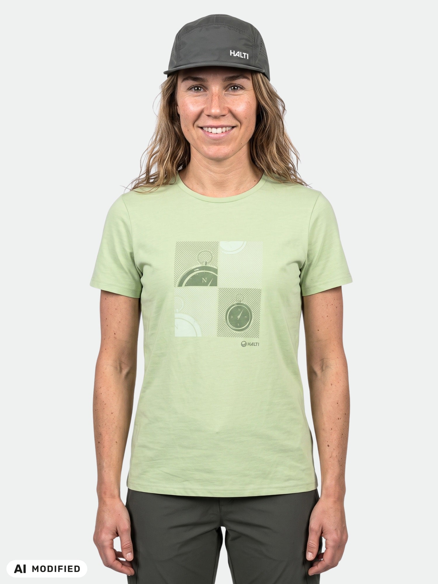 Eine Frau in einem hellgrünen Halti-Matka-T-Shirt, einer schwarzen Mütze und einer dunklen Hose steht vor einem schlichten, hellen Hintergrund.