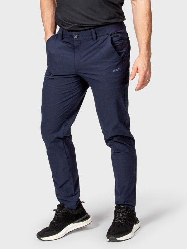 Eine Person steht mit den Händen in den Taschen und trägt Halti Drive Herren X-stretch Chinos in navy mit schwarzen Sportschuhen.