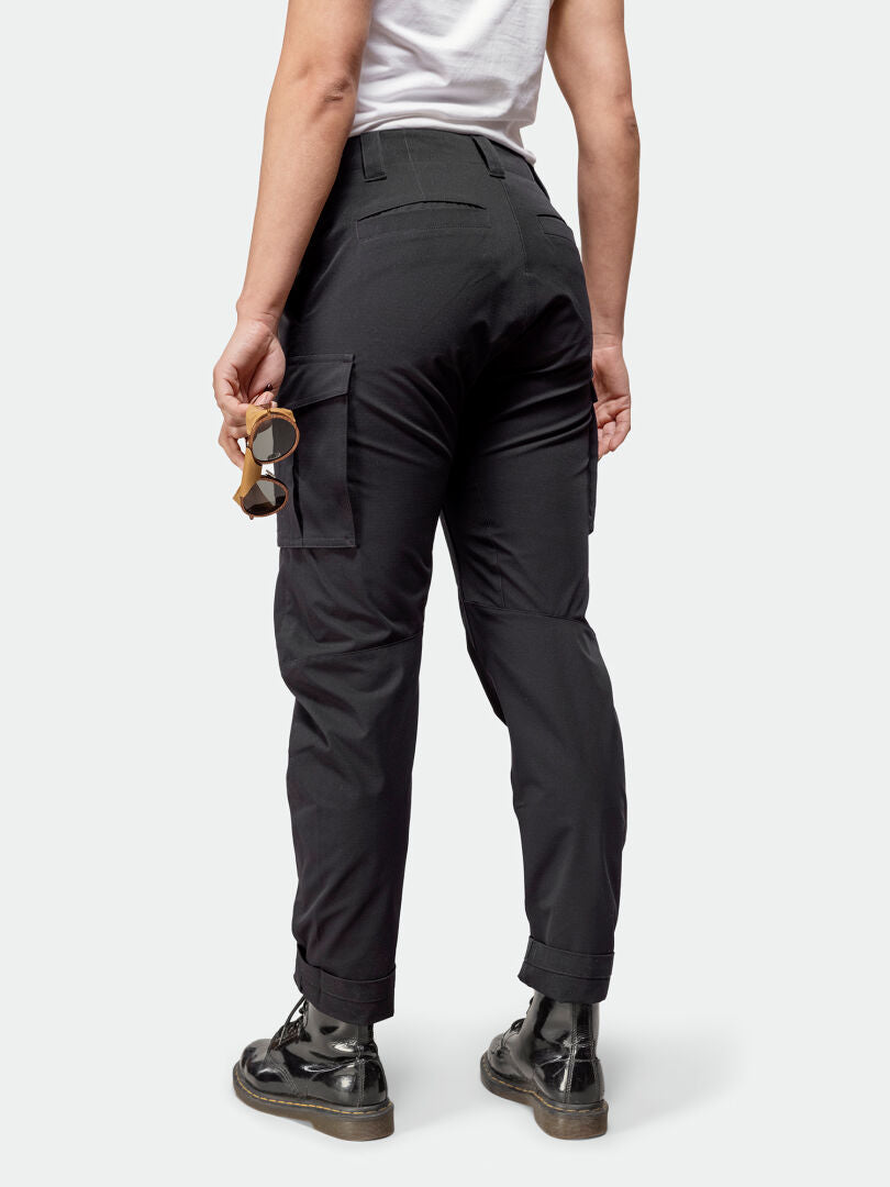 Frau trägt Halti Roams Cargo Hosen Damen aus elastischem Ripstop, schwarze Stiefel, weißes Shirt, Sonnenbrille in der Hand.