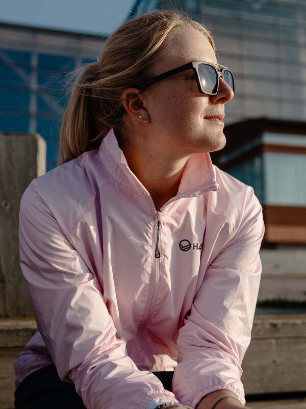 Eine Person in einer Halti Saime Windbreaker Jacke Damen aus recycelten Materialien sitzt draußen, die Sonne scheint ihr ins Gesicht.