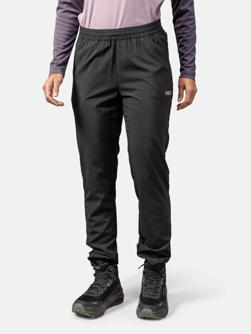 Das Model trägt Halti Grets Jogginghose Damen in Schwarz, ein lilafarbenes Top und schwarze Wanderschuhe vor einem weißen Hintergrund.